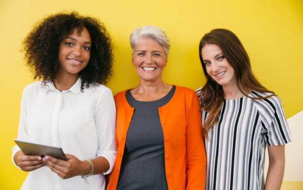 Three smiling women on a bright yellow backdrop